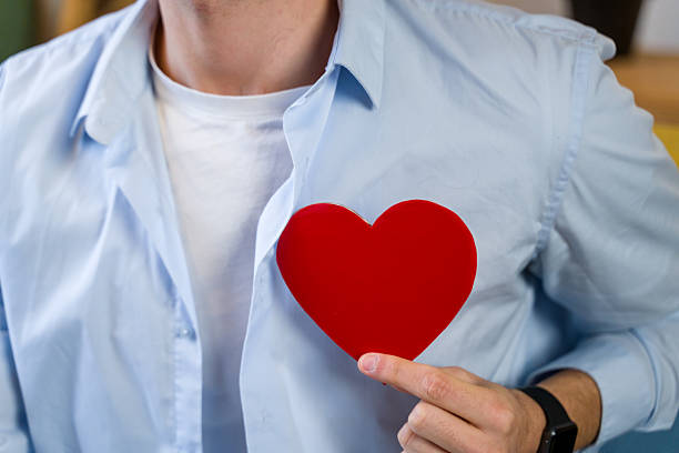 Man displaying a red heart shape, symbolizing love, health, and care