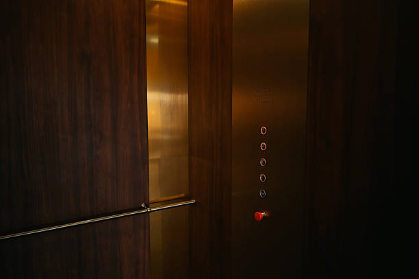 The silver and wooden elevator has a green button that says G. The door is open and the inside is empty