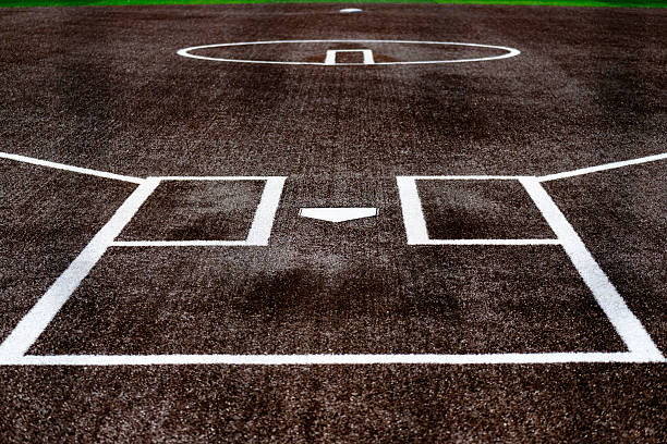 Groomed softball and baseball diamond at night.  Bright stadium lights illuminate the red sand and green grass field while darkness isolates the field from its surroundings.  No players on the field.