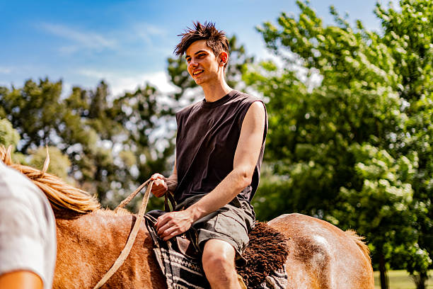 Young man horseback riding at a traditional ranch setting. The scene captures a relaxed tourist experience in a rural environment, highlighting leisure, travel, and countryside lifestyle