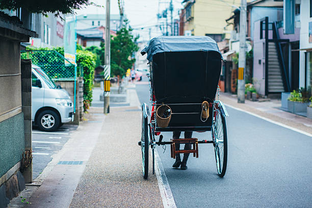 Traditional Japanese rickshaws lined up along a quiet road with mountains and greenery in the background in Japan. Travel and tourism scene capturing cultural heritage, slow travel, and traditional transportation in a peaceful natural setting. Selective focus with shallow depth of field.