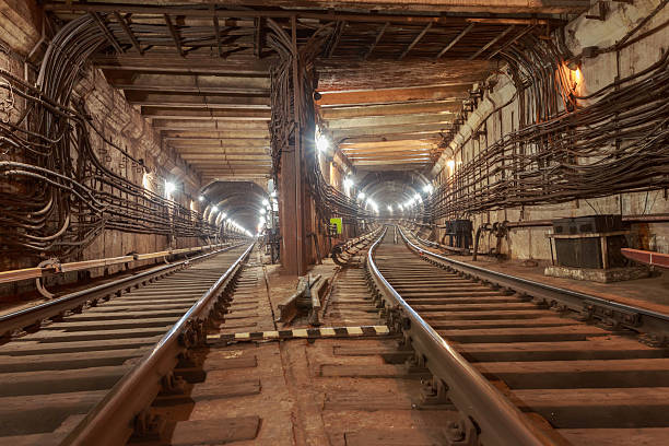 Close-up view of a subway tunnel between stations. The underground passage is illuminated by work lights along the walls.
