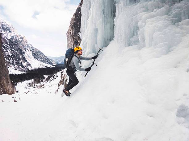 A climber ascending an icy wall in a mountainous landscape, wearing safety gear and using ice axes, showcasing adventure and determination