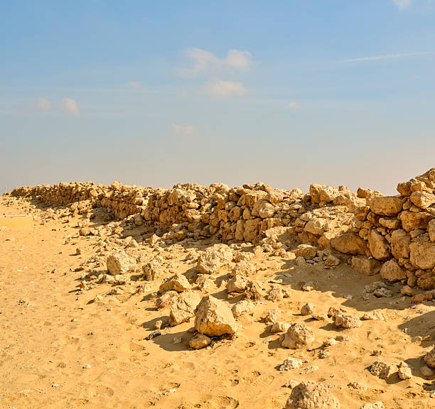 In this captivating image, an ancient stone wall extends across a golden sandy landscape, illuminated by sunlight under a clear sky. This serene view captures the historical essence and timeless beauty of Egypt.