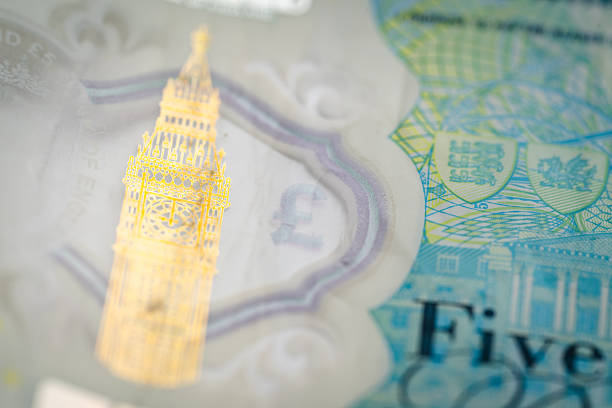 A macro photograph of a £5 British polymer banknote highlighting the golden Big Ben hologram and surrounding blue security elements. The image showcases the intricate design and anti-counterfeit features used in modern UK currency.
