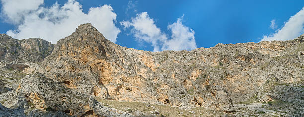 A striking Crete landscape in Greece showcasing sheer limestone cliffs, rocky terrain, and lush greenery. Dramatic rock formations rise above forested slopes, offering a rugged, adventurous outdoor scene perfect for travel, nature, and landscape photography.