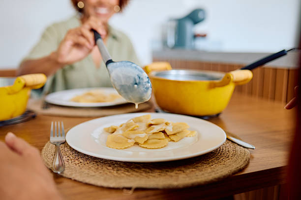 Woman serving hot ravioli pasta with creamy white sauce onto a plate, enjoying a homemade meal with family