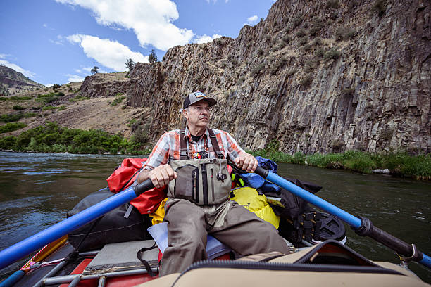 A fly fisherman rows a raft loaded with camping and fishing gear downstream through a dramatic canyon landscape while relocating camp during a multi-day fishing trip in Central Oregon.