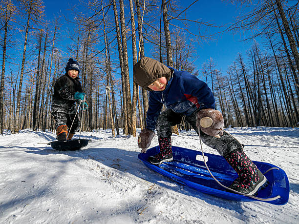 Two mongolian children play with sleds on fresh snow in a taiga forest, capturing winter childhood, outdoor adventure, and everyday life in a reindeer herder community. Tsagaannuur