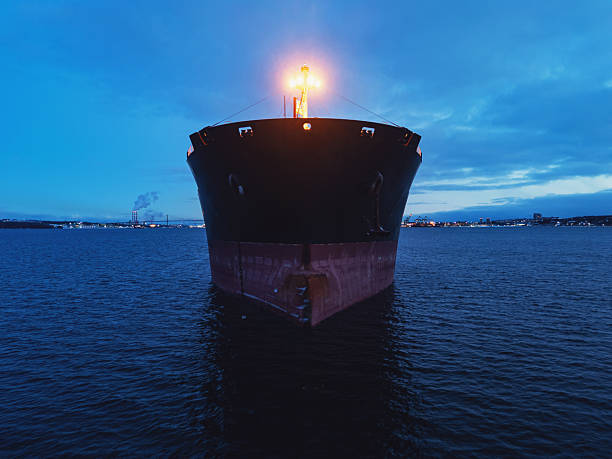 An overhead perspective of a large red cargo ship's bow as it navigates through the deep blue sea, leaving a white wake.