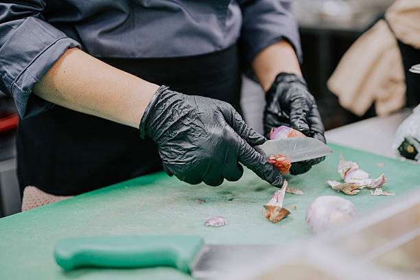 Close-up of asian female chef wearing black gloves slicing red onion on cutting board during restaurant food prep.