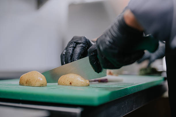 Close up of chef hands chopping potatoes on cutting board in commercial kitchen