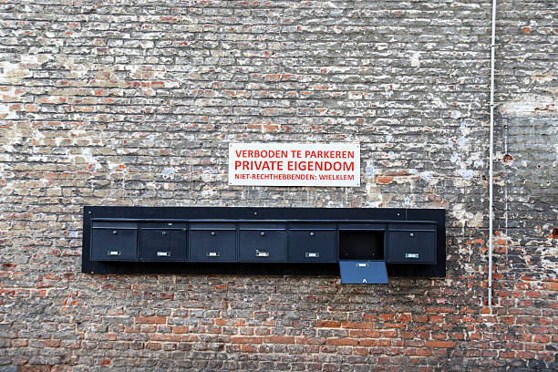 Seven residential mailboxes in a row on an old brick wall. A no parking notice is above.