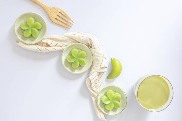 Top view of a green steamed pandan layer cake on small cups, served with a cup of green tea, a traditional Thai dessert. Close-up. Flat lay.