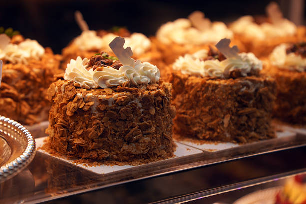 Close-up of beautifully decorated carrot cakes with cream frosting and crunchy toppings, displayed in a bakery or cafe setting, showcasing their delicious and appetizing appearance.