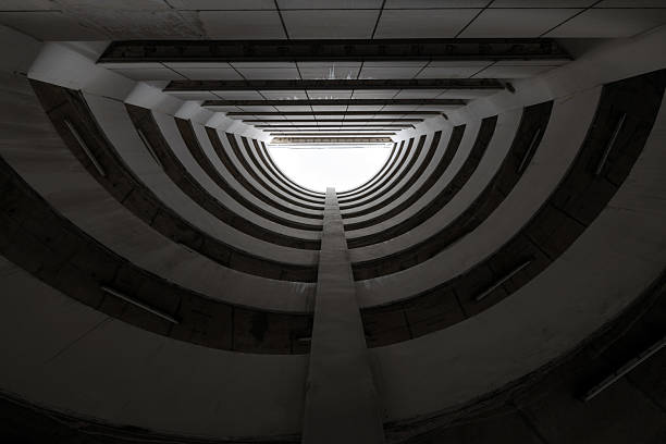 Bottom view of circular car parking garage against white clouds and blue sky. Automated circular parking system. Abstract architecture building.