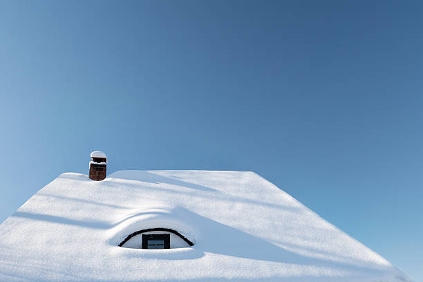 Minimal winter scene featuring a house roof completely covered in fresh snow with a small chimney and clear blue sky. Strong negative space and clean composition make this image ideal for winter, cold weather, home, insulation, energy, and seasonal concepts.