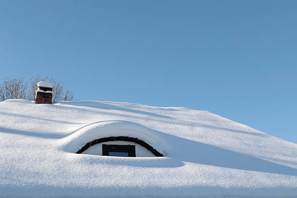 Minimal winter scene featuring a house roof completely covered in fresh snow with a small chimney and clear blue sky. Strong negative space and clean composition make this image ideal for winter, cold weather, home, insulation, energy, and seasonal concepts.
