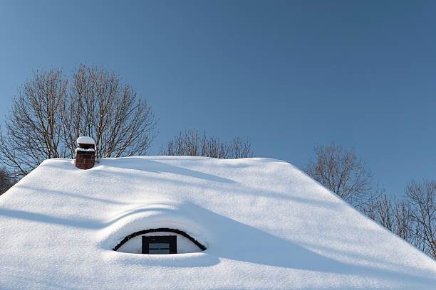 Minimal winter scene featuring a house roof completely covered in fresh snow with a small chimney and clear blue sky. Strong negative space and clean composition make this image ideal for winter, cold weather, home, insulation, energy, and seasonal concepts.