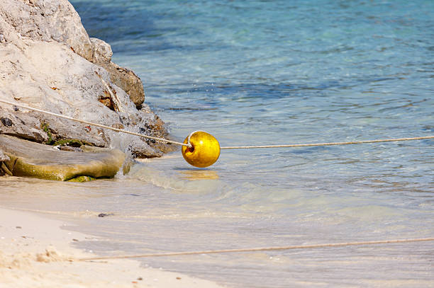 A yellow buoy is floating in the ocean. The buoy is tied to a rope