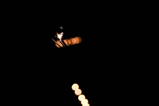 Close-up of a sparkler creating small glowing sparks in the dark night. Minimal light scene with warm bokeh background, suitable for celebration, abstract, and festive atmosphere concepts.