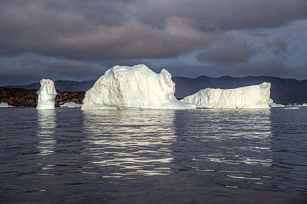 Towering icebergs floating calmly in the dark water of Ilulissat Icefjord, Greenland, presenting the fragile beauty of the Arctic environment and the ongoing impact of global warming