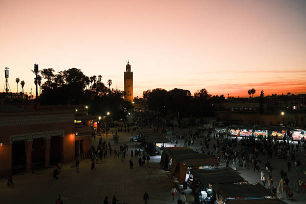 Jemaa el-Fnaa square bustling with activity during a vibrant sunset, Koutoubia Mosque minaret visible in the distance