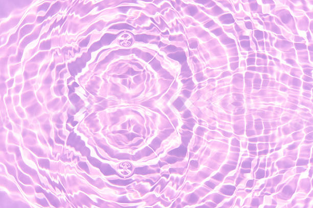 Purple water bubbles on the surface ripples. Defocus blurred transparent pink colored clear calm water surface texture with splash and bubbles. Water waves with shining pattern texture background