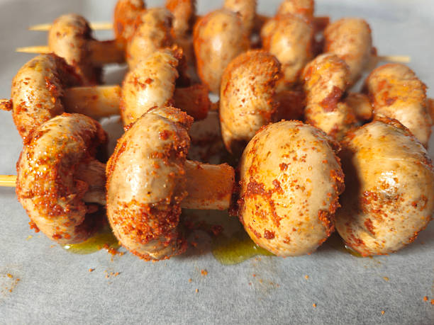 Champignon mushrooms coated with spices on bamboo skewers, prepared for baking in the oven. Homemade vegetarian food preparation
