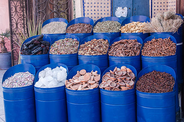 Colorful display of traditional spices and dried herbs in blue barrels at a local Moroccan market. The vibrant assortment includes cinnamon sticks, cloves, resins, dried plants and herbal mixtures, reflecting the rich culinary and cultural heritage of Morocco.