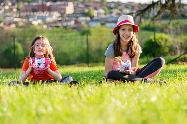 Two smiling elementary age girls sitting on green grass, holding Easter baskets and treats during an outdoor hunt