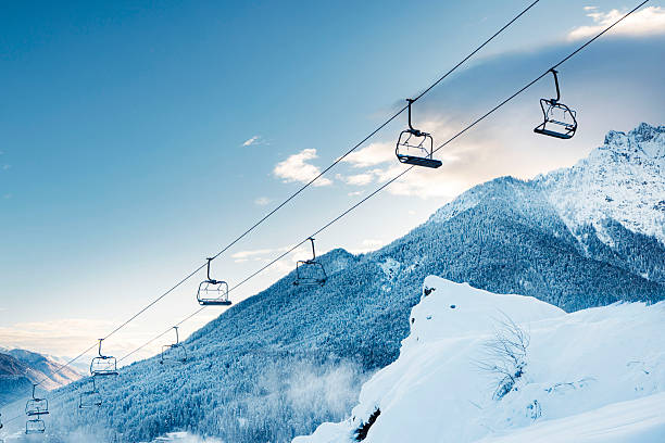 Ski lift chairs suspended over snowy mountain landscape at sunrise.