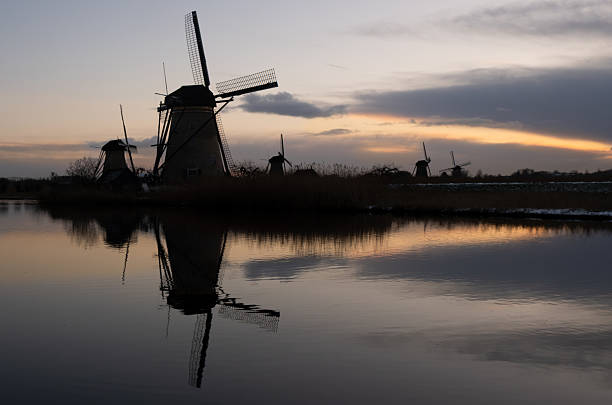 Kinderdijk Windmills standing along a tranquil canal, their reflections visible in the water, capturing the unique dutch unesco landscape in winter at sunset. Netherlands