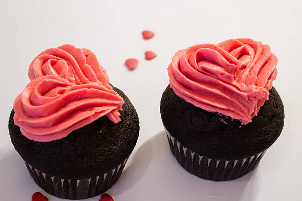 Two beautiful chocolate cupcakes decorated with pink frosting hearts on a white background,  perfect for valentine's day