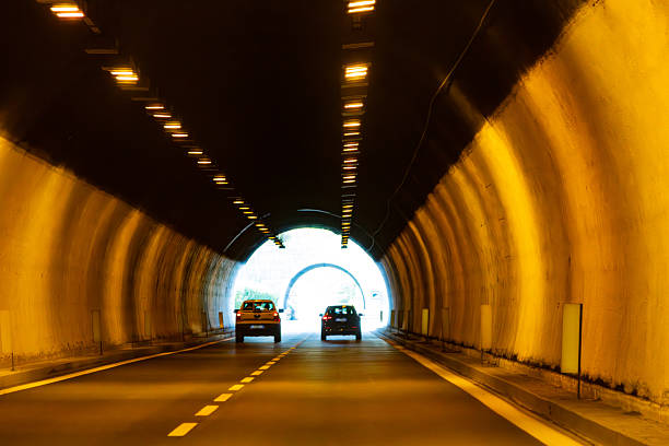 Parma, Italy, September 7, 2025: Two vehicles move along a paved roadway within a tunnel that features reflective signs and a view of the outside at the end.