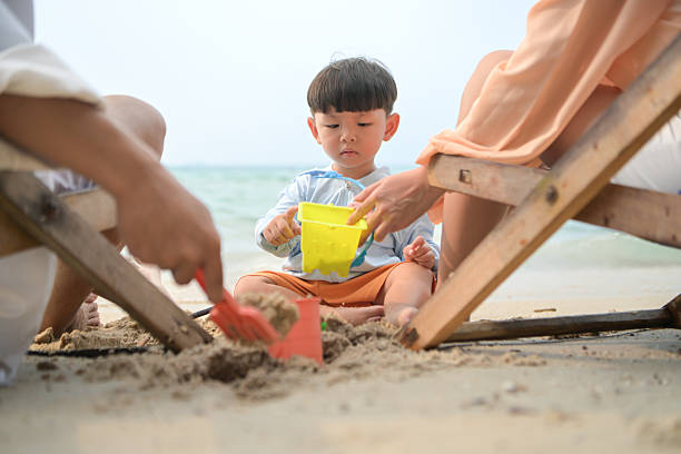 In holiday, Parents sitting on beach chairs while watching their young child playing with sand toys on the beach during daytime
