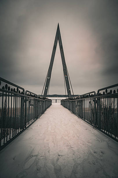A geometric viewing platform in winter with a blanket of snow along the path under a grey sky, hiking in snow and icy temperatures around the Thülsfeld reservoir, Cloppenburg, Lower Saxony, Germany