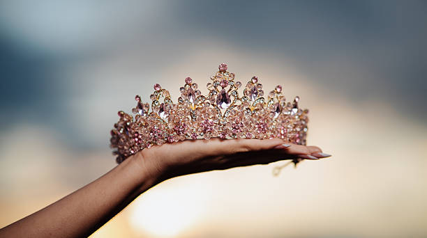 A woman's hand holding a princess crown at sunset
