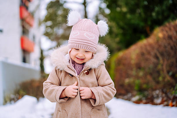 Smiling toddler girl walking outdoors during winter, surrounded by snow and bare trees.