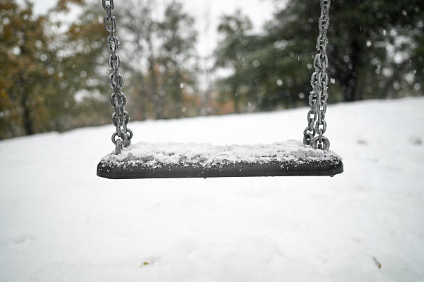 Empty playground swing covered in fresh snow on a cold winter day