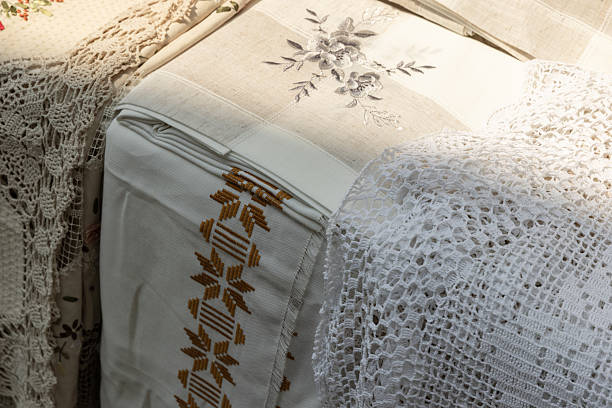 A close-up of vintage linen fabrics featuring brown embroidery patterns and delicate white crochet lace. Warm, soft lighting highlights texture and craftsmanship, conveying cozy handcrafted home decor