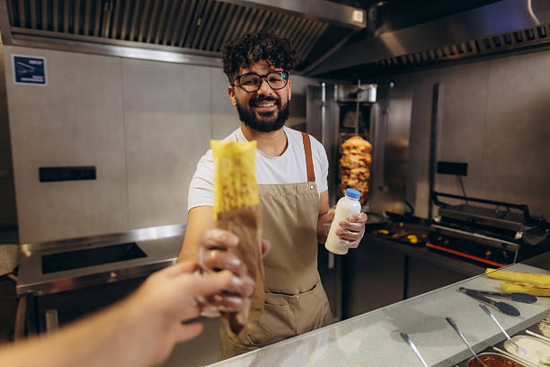 Smiling chef serving street food kebab or shawarma wrap to customer in a fast food restaurant kitchen