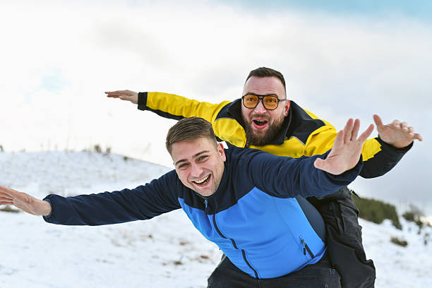 Joyful gay couple having fun outdoors on a snow-covered mountain. Bright clothing and expressive faces capture happiness, freedom, and winter travel lifestyle.