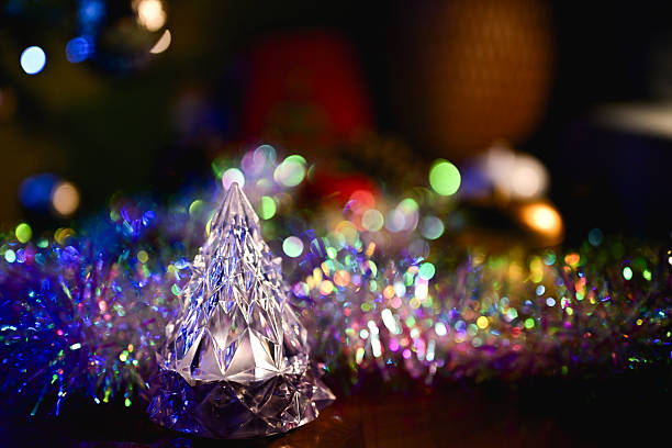 Crystal tree ornament reflecting colorful bokeh from festive Christmas lights and tinsel