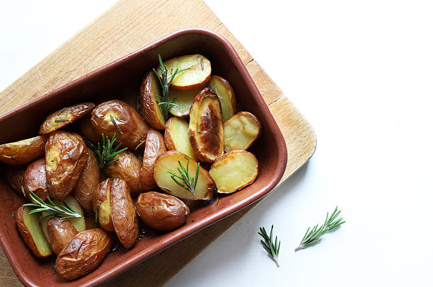 Oven baked new red potatoes, cut in half, with rosemary sprigs and olive oil, just from the oven on a white background. Healthy and vegetarian food. Overhead view.