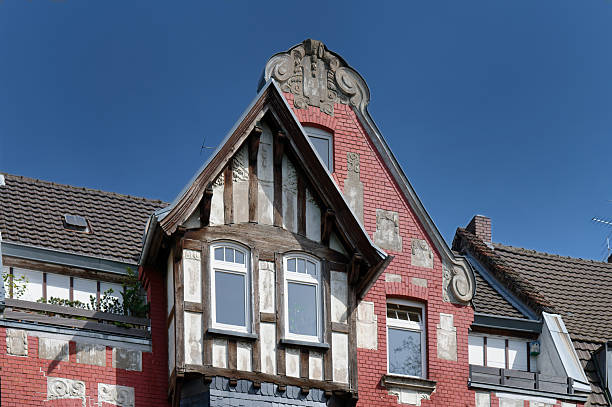 Eclectic historic house facade in Cologne featuring red brickwork, a half-timbered bay window, and an ornate baroque gable. Unique urban detail