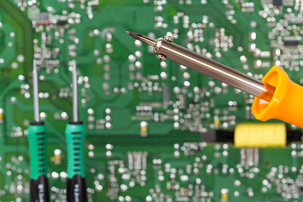A close-up of an electrical circuit board with a soldering iron and screwdrivers