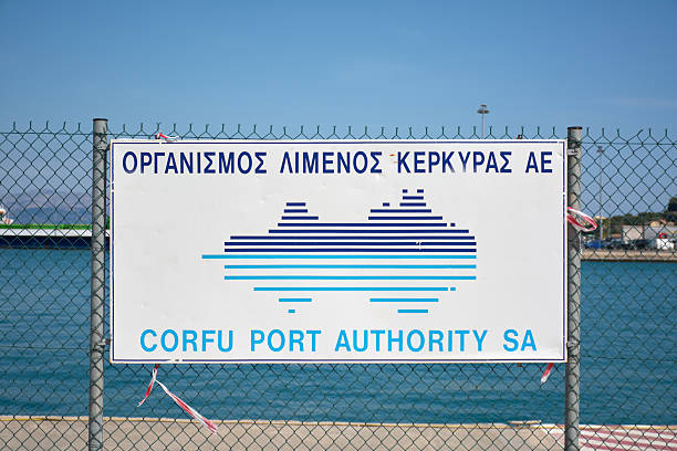 Corfu. Greece - January 29, 2026: corfu port authority sign mounted on a fence beside the harbor, with calm blue water and clear sky, representing maritime governance, transport infrastructure, and regional logistics