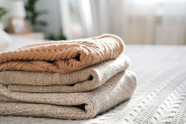 istock Stack of cozy folded knitted sweaters in neutral beige and cream tones on bed. Concept of hygge, winter comfort, slow living and organized home wardrobe 2258909624