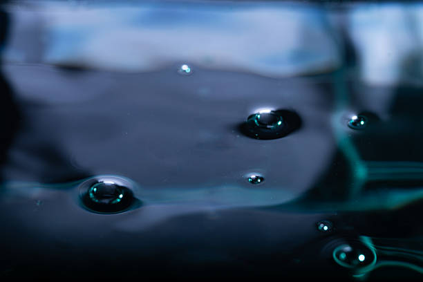 279.Raised bubbles scatter across glossy dark viscous liquid. Blue-green reflections and blurred background enhance fluid texture, surface tension, and abstract composition.